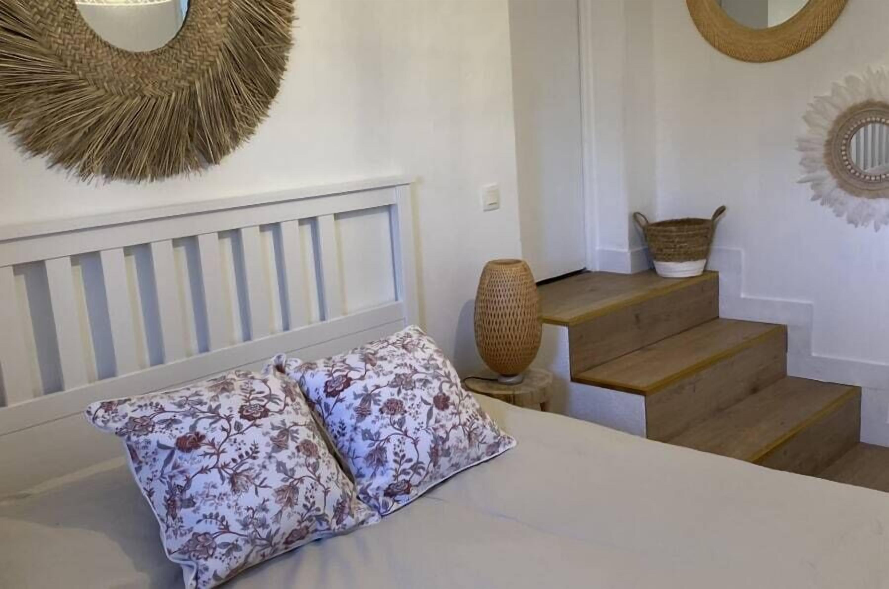 A bedroom with a bed, two floral pillows, a woven basket, and a woven wall decoration.