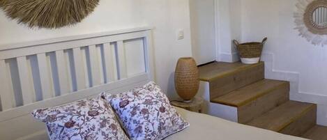 A bedroom with a bed, two floral pillows, a woven basket, and a woven wall decoration.