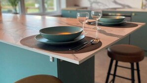 Une cuisine moderne avec un plan de travail en marbre, un saladier de couleur turquoise, des verres à vin et un tabouret de bar.