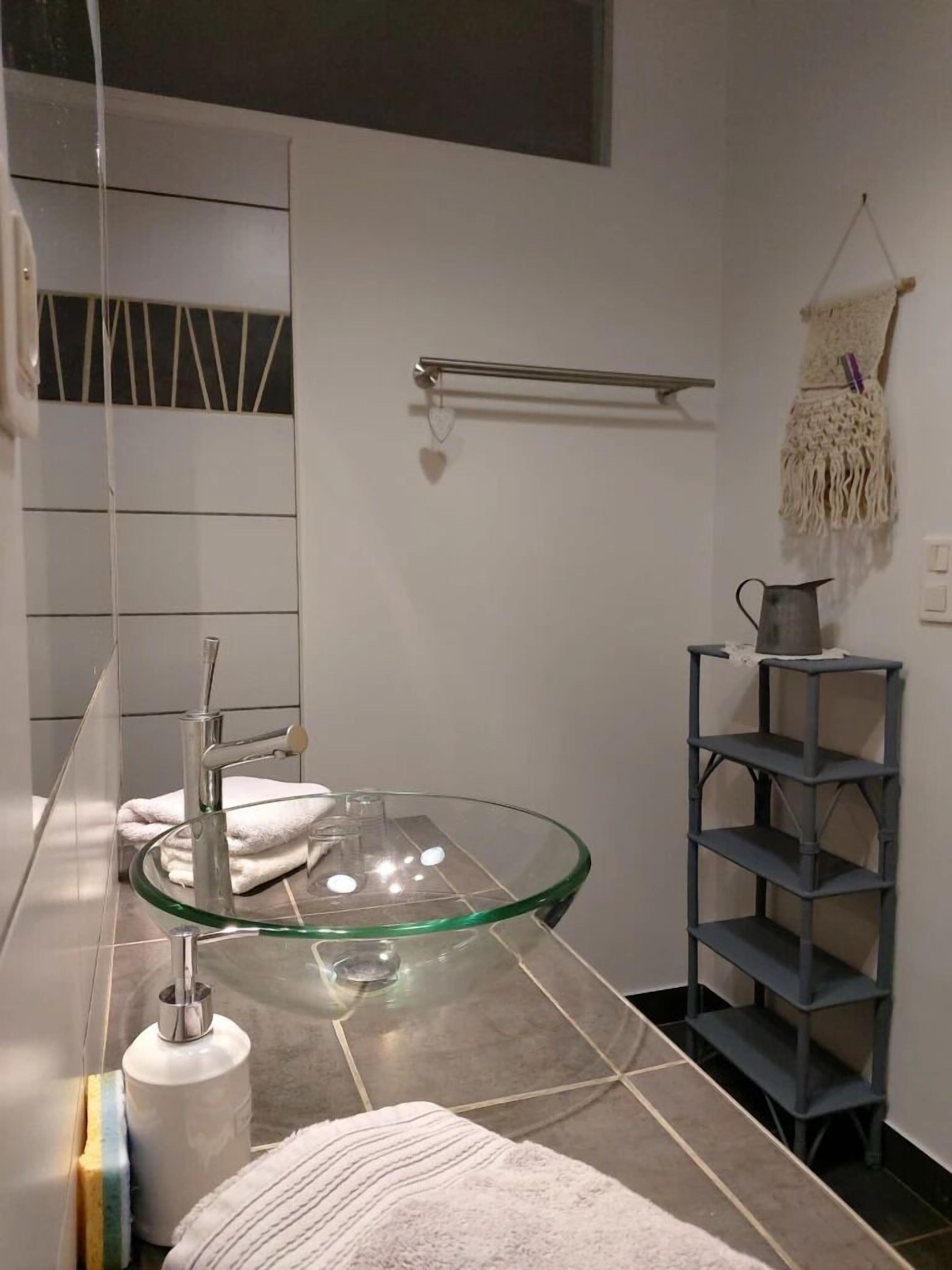 Une salle de bain moderne avec un lavabo en verre, un porte-serviettes, une étagère et un support à papier toilette.