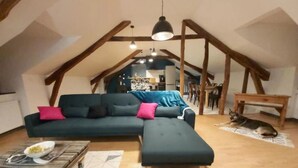 A cozy loft-style living room with a sectional sofa, a dining table, and a dog resting on a rug. - Le Saint-Georges (Villefranche-de-Rouergue)