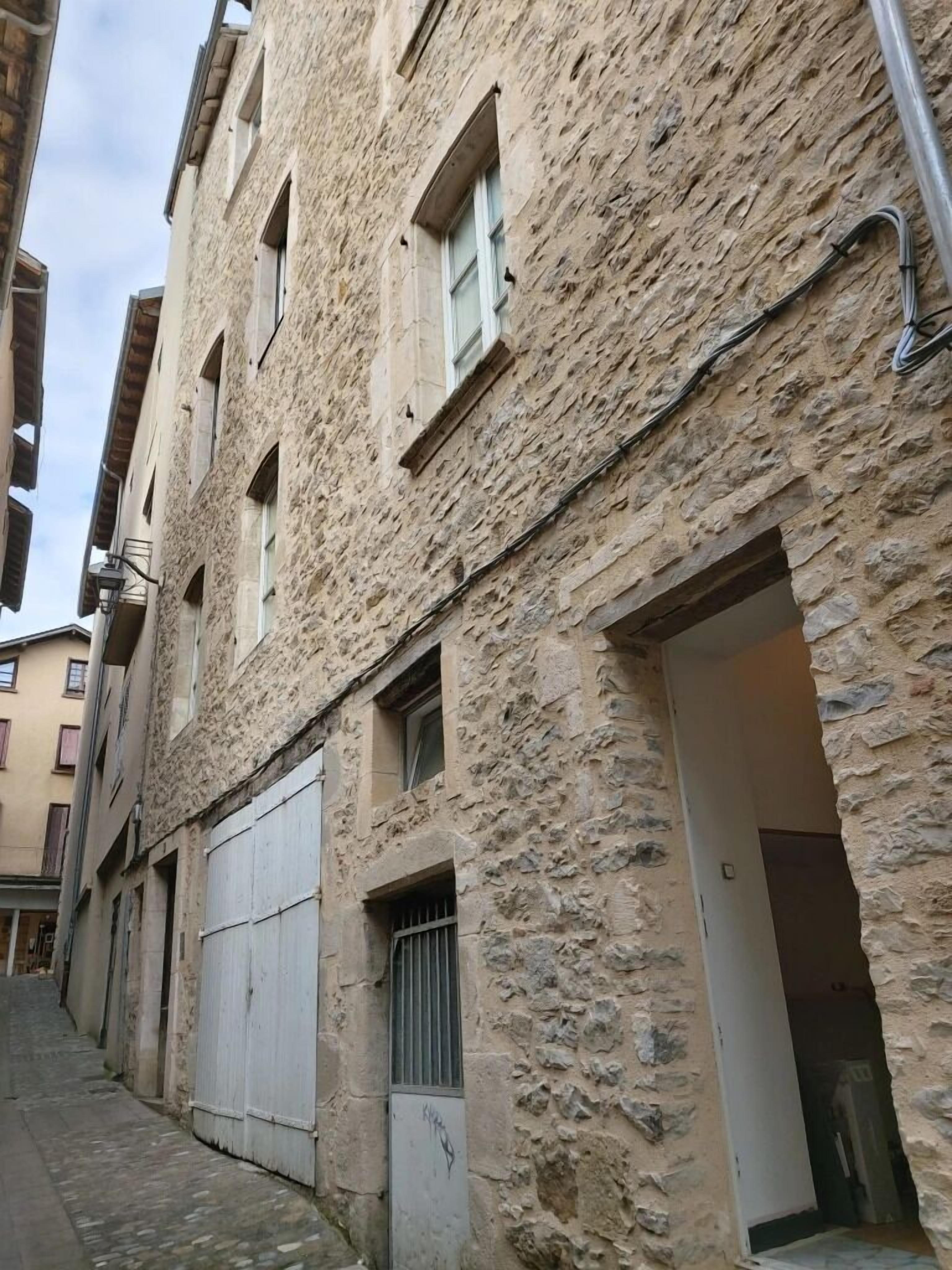 A narrow street with stone buildings, a closed garage door, and a metal gate.