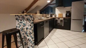 A modern kitchen with a central island, dark cabinetry, and a geometric backsplash. - Le Saint-Georges (Villefranche-de-Rouergue)