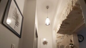 A narrow hallway with a framed picture on the left, a light fixture in the center, and a stone wall on the right. - Le Saint-Georges (Villefranche-de-Rouergue)