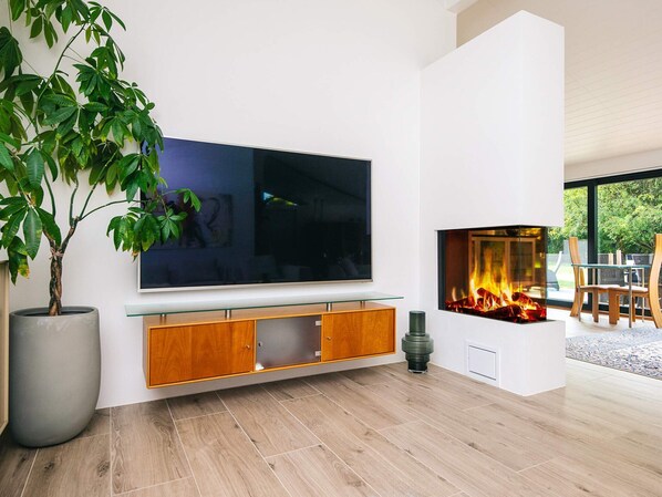 A modern living room with a large flat-screen TV, a built-in fireplace, and a potted plant.