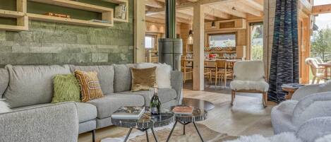 A spacious living area with a grey sofa, a coffee table, and a fur rug. There are wooden shelves above the sofa and a dining area in the background.