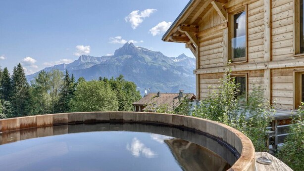 A wooden cabin with a hot tub and a mountain view.