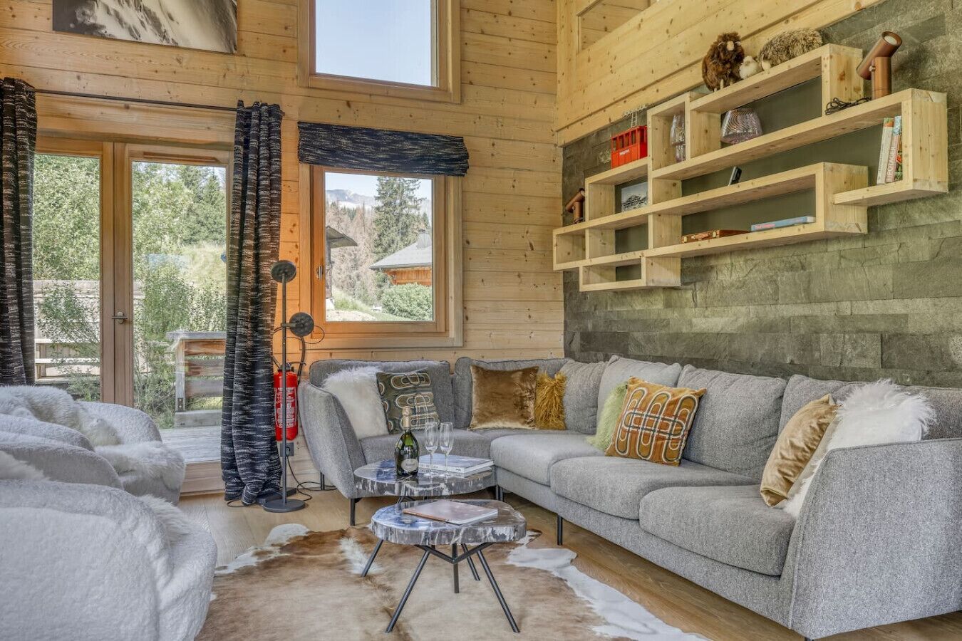Un salon chaleureux avec un canapé gris, une table basse et un tapis en fourrure. On y trouve des étagères en bois ornées de livres et d’objets décoratifs.