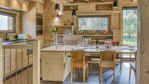 A wooden cabin kitchen with a central island, wooden cabinets, and a window overlooking greenery.