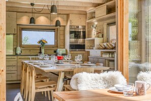 Interior de una cabaña de madera con comedor, cocina y un ventanal grande.