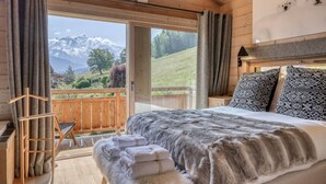 A bedroom with a large bed, a wooden headboard, and a view of mountains through a sliding door.