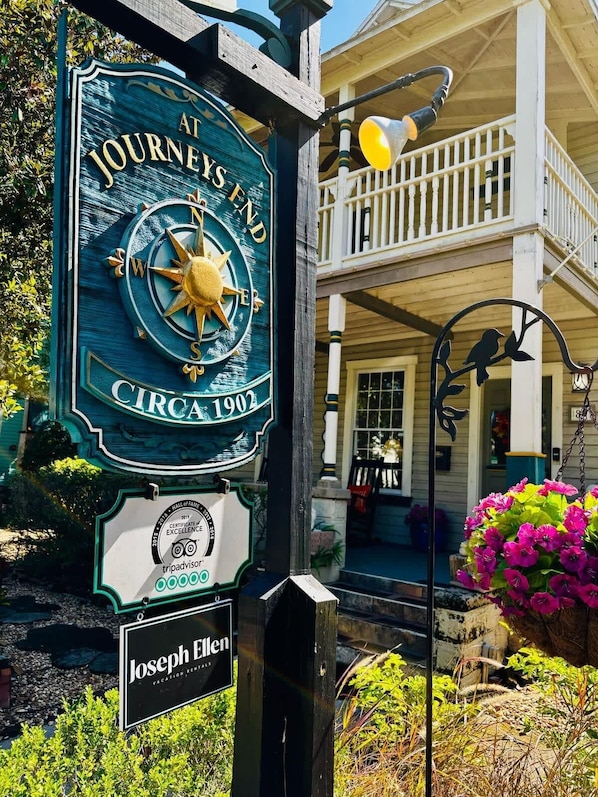 A sign for 'At Journeys End' with a compass, a TripAdvisor certificate, and a 'Joseph Ellen Vacation Bungalows' sign.