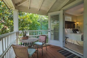 A covered porch with a table and chairs, a potted plant, and a view of a bedroom with a bed and a lamp. - Amelia Earhart Room | Team Joseph Ellen (St. Augustine)