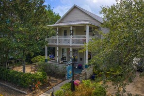 Une maison à deux étages avec un balcon, entourée d’arbres et d’un jardin.