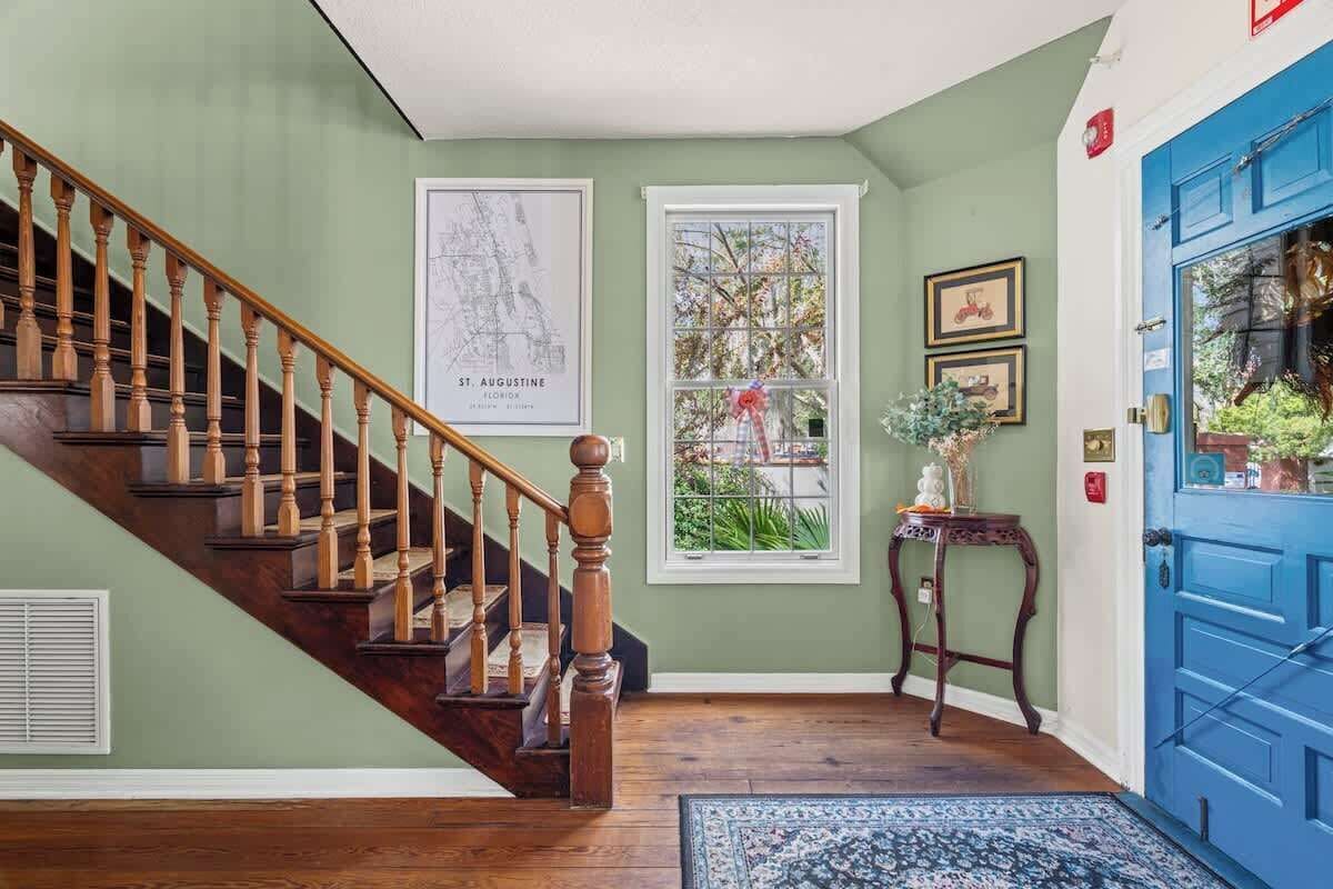 A staircase with wooden balusters, a blue door, a window with a view, and a framed map on the wall.
