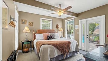 A bedroom with a bed, ceiling fan, bedside lamps, a small table, and a view through the door.