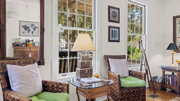 A room with wicker chairs, a glass table, and large windows with a view of greenery.