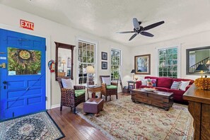 Un salon avec une porte bleue portant l’inscription « SORTIE », un ventilateur de plafond et un canapé rouge.