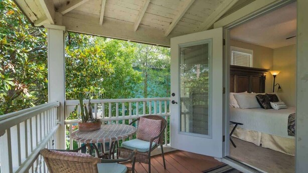 Eine überdachte Veranda mit Tisch und Stühlen, einem Blumentopf und Blick auf ein Schlafzimmer mit Bett und Lampe.
