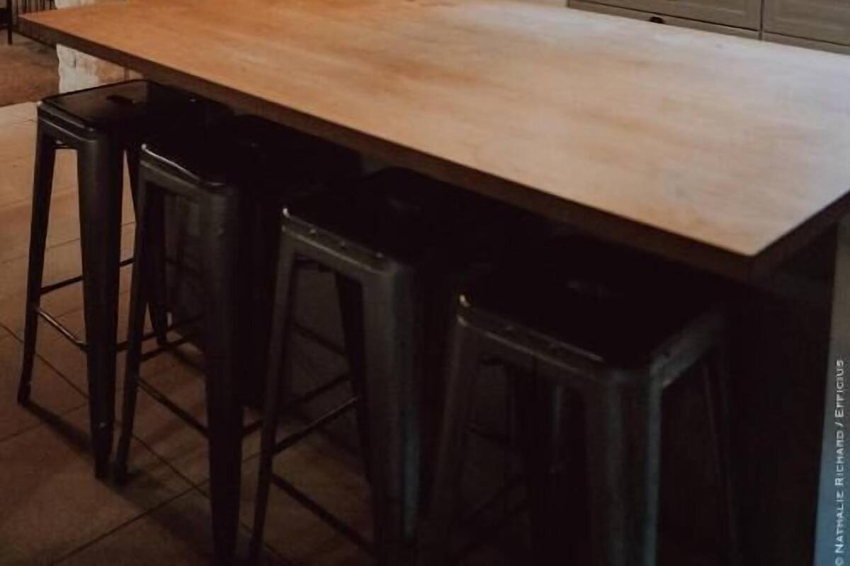 A rustic kitchen with exposed wooden beams, a long island with stools, and various kitchen appliances and storage jars.