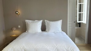 Ein ordentlich bezogenes Bett mit weißen Leinen in einem schlicht und modern eingerichteten Raum.