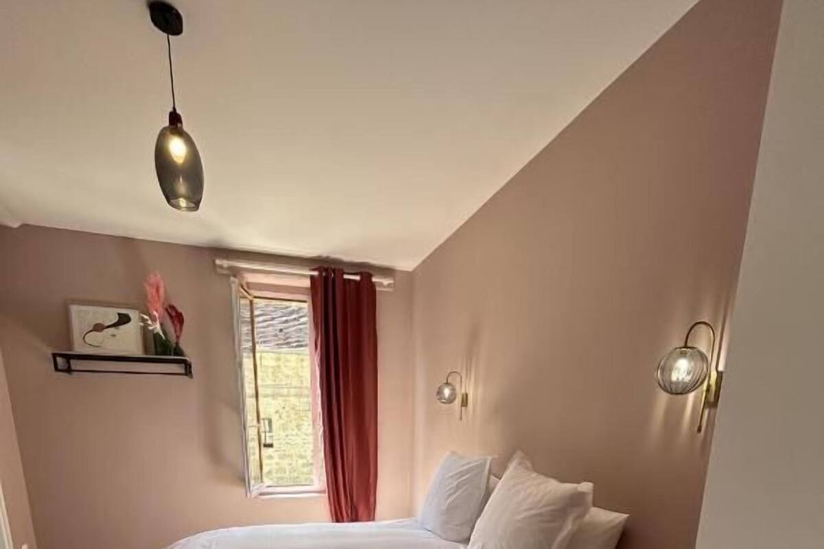 Ein Schlafzimmer mit einem Bett, einem Fenster mit Vorhängen, einem an der Wand befestigten Regal und einer Tür mit Griff.