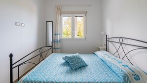 Een slaapkamer met een bed, een raam, een nachtkastje en een spiegel.