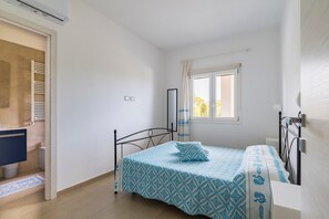 A bedroom with a bed, a window, a wardrobe, and a bathroom. - Villa Giustina - Apartment (Tortolì)