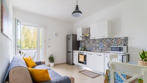 Een compacte leefruimte met een kitchenette, een bank met kussens, een eettafel en een potplant.