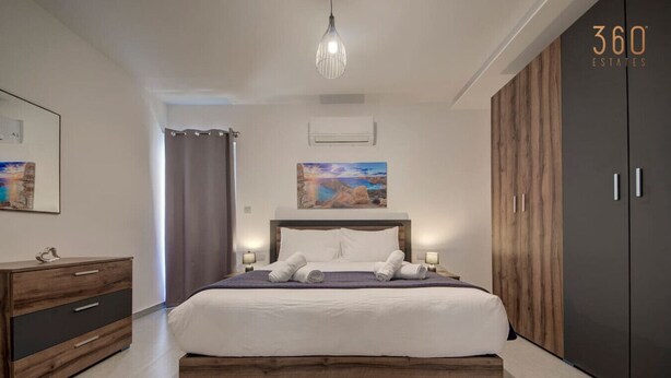 A modern bedroom with a large bed, wooden headboard, a nightstand, a dresser, and a wardrobe. - Central Comfort: Stylish 2BR Apt with Balconies! (Qormi)