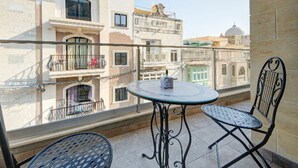 A balcony with a round table and two chairs, overlooking a cityscape with historic buildings. - Central Comfort: Stylish 2BR Apt with Balconies! (Qormi)