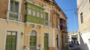 A narrow street with historic buildings, green doors, and a clear sky. - Central Comfort: Stylish 2BR Apt with Balconies! (Qormi)