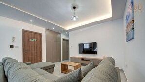A modern living room with a sofa, a coffee table, a TV, and a door marked "Exit". - Central Comfort: Stylish 2BR Apt with Balconies! (Qormi)