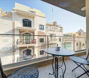 Un balcone con un tavolo rotondo e due sedie, affacciato su una città con edifici storici.