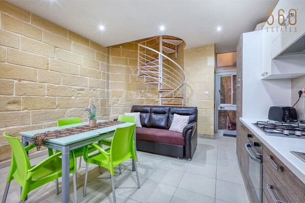 Un espace de vie compact comprenant un coin repas, un canapé, un escalier en colimaçon et une petite cuisine.