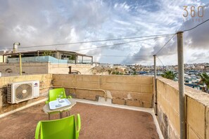 Une terrasse sur le toit, avec une table et des chaises, d’où l’on peut admirer une vue panoramique sur la ville, avec ses bâtiments et son port.