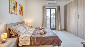 A hotel room with a bed, bedside lamps, artwork on the wall, an air conditioning unit, and a view through the window. - Seaview Marsaxlokk Townhouse, steps from Market! (Marsaxlokk)