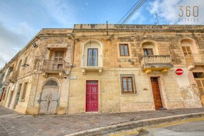 Un bâtiment historique avec une porte rouge, des fenêtres en arc de cercle et un balcon.