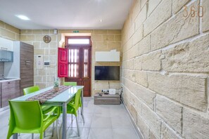 Une cuisine compacte avec un coin repas, une horloge et un téléviseur fixé au mur.