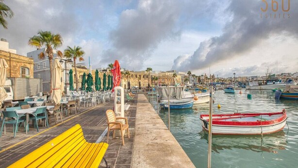 A waterfront café with outdoor seating, a wooden bench, and a row of umbrellas. - Seaview Marsaxlokk Townhouse, steps from Market! (Marsaxlokk)