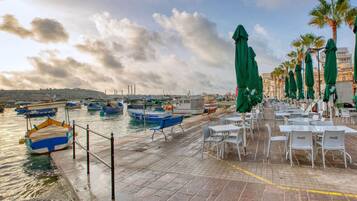 A waterfront café with outdoor seating, boats docked nearby, and a clear sky.