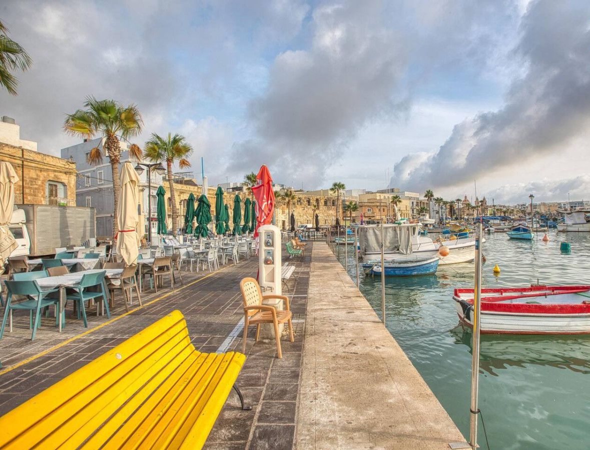 Un café situé au bord de l’eau, avec une terrasse, un banc en bois et une rangée de parasols.