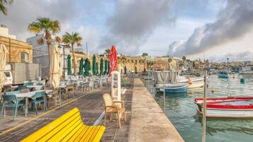 A waterfront café with outdoor seating, a wooden bench, and a row of umbrellas.