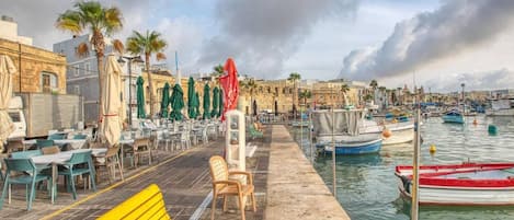 Un café situé au bord de l’eau, avec une terrasse, un banc en bois et une rangée de parasols.