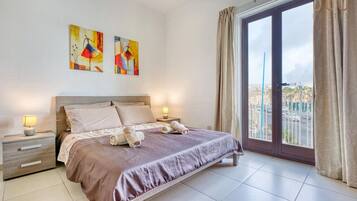 A bedroom with a large bed, a nightstand, a window with curtains, and two wall-mounted paintings.