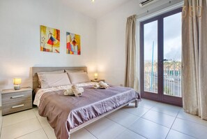 Une chambre à coucher avec un grand lit, une table de chevet, une fenêtre avec des rideaux et deux tableaux accrochés au mur.