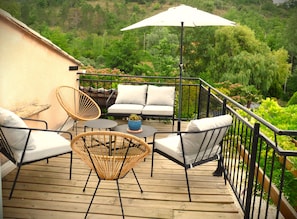 Una terraza de madera con mobiliario exterior, incluyendo sillas de mimbre y un sofá, además de un paraguas grande.