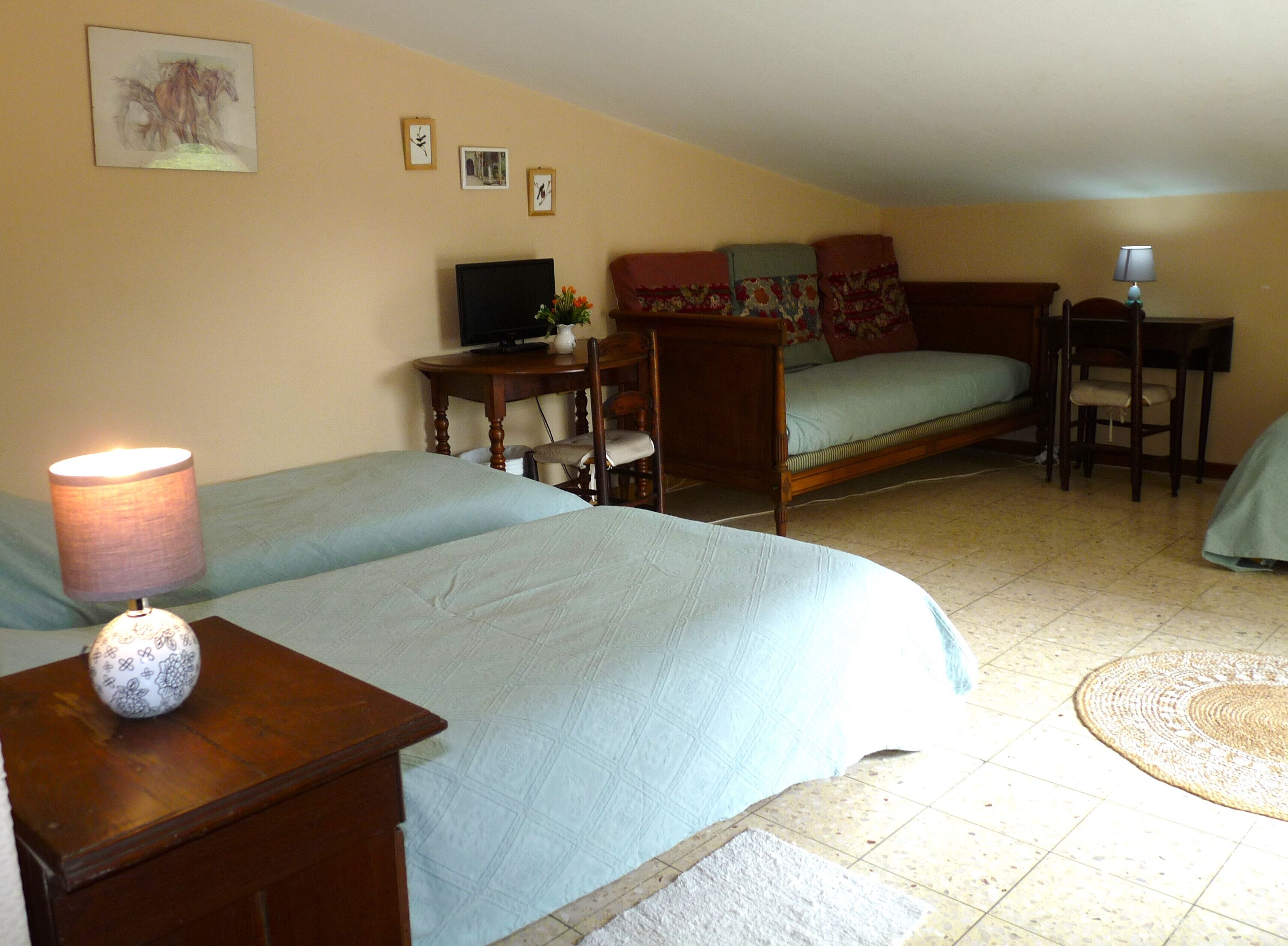 A bedroom with two beds, a desk, a chair, a television, and a lamp.