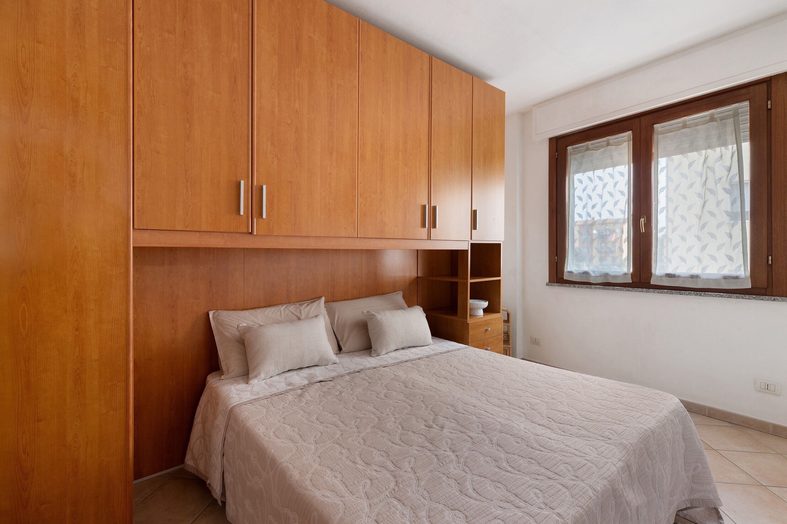 Un dormitorio con cama, armario de madera y ventana con cortinas estampadas.