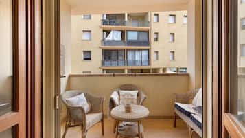 Un balcon doté de meubles en osier, notamment des chaises et une petite table, donnant sur un immeuble comportant de nombreux balcons.